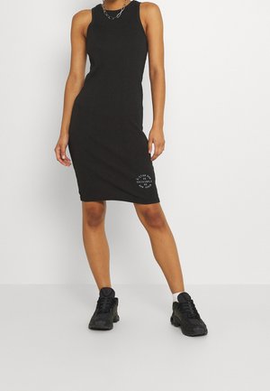 Czarna prążkowana sukienka na ramiączkach o dopasowanym kroju, z długością do kolan i białym logo blisko dołu sukienki. Noszona z czarnymi trampkami.