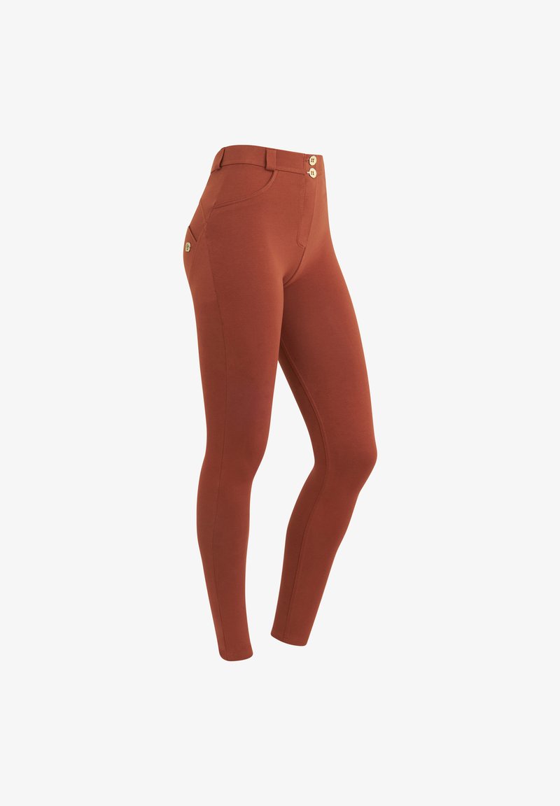 Leggings color ruggine con una texture liscia, caratterizzati da un alto elastico in vita e due bottoni frontali. Dettaglio della tasca laterale visibile.