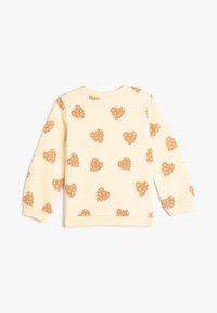 Kremowy sweatshirt z powtarzającym się wzorem pomarańczowych serc w białe kropki, okrągły dekolt i ściągacze przy rękawach.