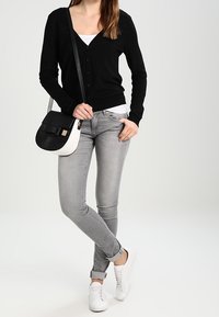 Svart cardigan med V-ringning och knappar, vit tanktop, grå jeans, vita sneakers och en svart och vit handväska med rosettdetalj.
