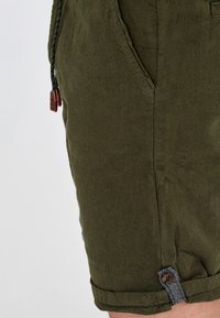 Shorts vert olive en tissu texturé, avec poches latérales, ourlet retroussé orné d'un bouton marron et d'un cordon tressé.