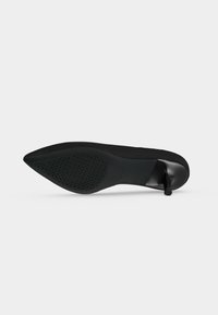 Chaussure à talon haut noire vue de la semelle, avec un bout pointu et une accroche texturée sur la moitié avant de la semelle.