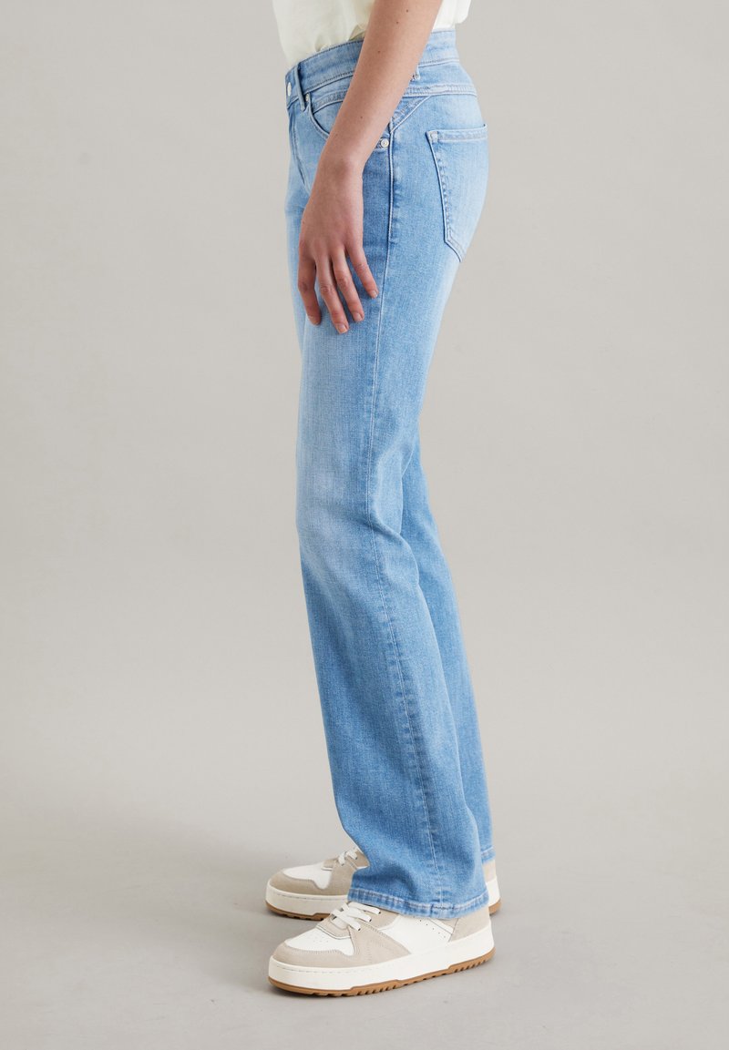 Jasnoniebieskie dżinsy o prostym kroju, średnim stanie i dwóch tylnych kieszeniach. Połączone z białymi i beżowymi trampkami.