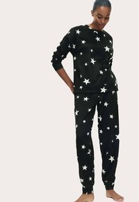 Pijama de forro polar negro con estampado de estrellas blancas por toda la prenda, con cuello redondo y mangas largas en la parte superior, y pantalones con cintura elástica.