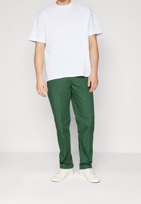 White cotton t-shirt with short sleeves, paired with green cotton trousers. White sneakers with a textured surface complete the outfit.