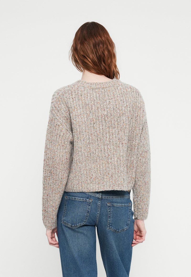 Lichtgrijze gebreide trui met een ronde hals en lange mouwen, voorzien van subtiele kleurrijke spikkels, gecombineerd met blauwe denim jeans.