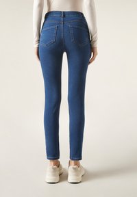 Smala jeans i mörkblå denim med en mjuk textur, femfickorsdesign och hög midja, i kombination med beige träningsskor.