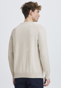 Lys beige strikkegenser med rund hals, lange ermer, ribbede mansjetter og midje. Glatt tekstur, enkelt design.