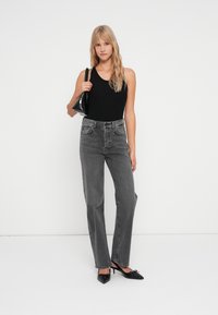 Jean gris taille haute avec une jambe droite, coutures détaillées et poches avant, associé à un haut sans manches noir et des chaussures noires.