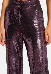 Purpurowe spodnie z cekinami o szerokim kroju. Posiadają odbijające światło cekiny, gładką fakturę oraz dopasowaną talię z zapięciem na guzik.
