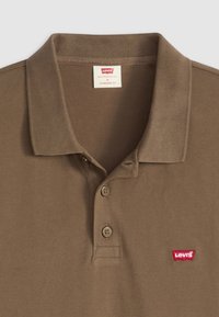Bruine polo gemaakt van textuurstof, met een kraag, twee knopen en een klein rood Levi's-logo op de linkerborst. Standaard pasvorm.