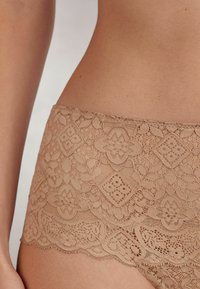 Koronkowe majtki hipster w kolorze nude, z kwiatowymi wzorami, falbaniastymi krawędziami oraz miękką, delikatną fakturą. Zaprojektowane z myślą o komforcie i stylu.