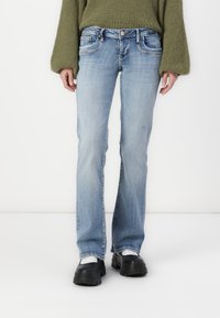 Hellblaue Denim-Jeans mit weitem Schnitt, Fronttaschen, subtilen Abriefungen und Kontrastnähten. Kombiniert mit klobigen schwarzen Plateauschuhen.