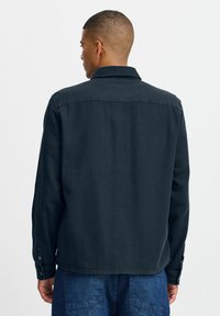 Dark denim jacket with a collared neck, buttoned cuffs, and a straight cut. Features plain texture and minimal detailing, presented from the back.