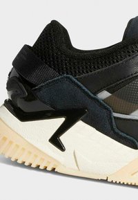 Black sneaker with a mix of mesh and suede materials, featuring a glossy black accent and a textured off-white sole with a zigzag design.