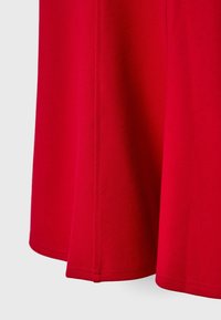 Panneau de tissu rouge vif avec une couture verticale visible et un détail d'ourlet sur un fond gris clair.