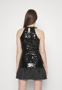 Robe noire pailletée avec un col halter, un dos en trou de serrure et un ourlet en tissu noir froncé. Texture brillante grâce aux paillettes.