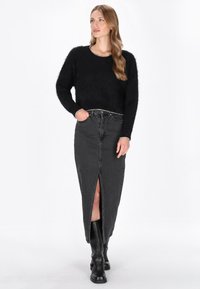 Czarny puszysty sweter wykonany na drutach z okrągłym dekoltem oraz srebrnymi akcentami, zestawiony z jasną spódnicą z ciemnego denimu o wysokim stanie, z rozcięciem.