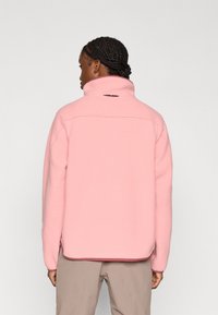 Ροζ φλις μπουφάν με ψηλό γιακά, υφή με ανάγλυφη επιφάνεια και πλαϊνές σχισμές για ευκολία στην κίνηση. Διαθέτει μικρό λογότυπο στο πίσω μ έρος.