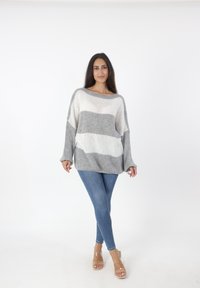 Lichte, gebreide trui met horizontale grijs-witte strepen. Ontspannen pasvorm, brede bootnek en verlaagde schouders. Gekleed met blauwe jeans.