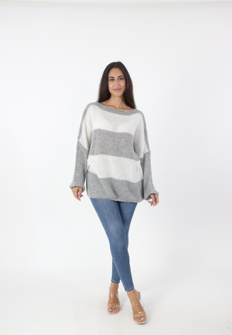 Suéter ligero de punto con rayas horizontales en gris y blanco. Corte relajado, amplio escote barco y hombros caídos. Combinado con jeans azules.