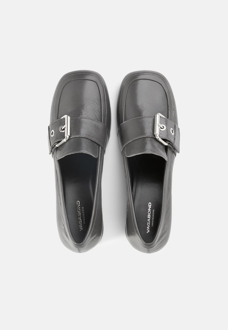 Black leather slip-on shoes featuring a rounded toe, flat sole, and a decorative buckle detail on the side. Smooth texture and minimal design.