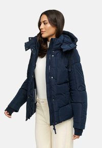 Navy blue puffer jacket with a detachable hood, front zipper, and snap buttons. Features elastic cuffs and a quilted texture.