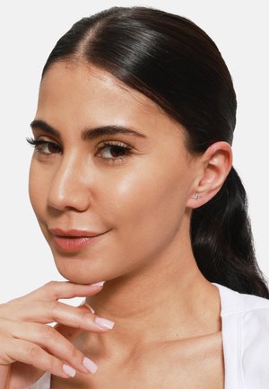 Boucles d'oreilles en forme d'étoile argentée avec une finition polie, portées dans une oreille percée. Texture lisse, petite taille et design minimaliste.