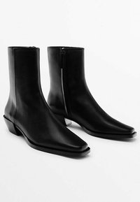 Stivali alla caviglia in pelle nera con punta affusolata, design elegante, zip laterale e tacco blocco basso. Texture liscia e accenti hardware minimi.