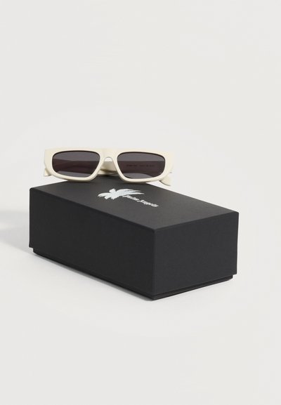 Lunettes de soleil rectangulaires blanches avec des verres foncés reposant sur une boîte noire ornée d'un logo de palmier blanc.