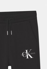 Svarta sweatpants med elastisk midja, snöre och sidofickor. Har en vit "Calvin Klein Jeans" logotyp. Slät bomullstextur.