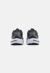Sneakers con una toma in rete grigia, colletto imbottito e suole bianche con accenti blu. La vista posteriore mostra il passante per la presa e il dettaglio del logo.