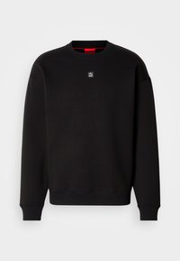 Sudadera negra de tejido suave con cuello redondo, puños acanalados y un pequeño logotipo cuadrado en el pecho. Presenta un interior del cuello en rojo.