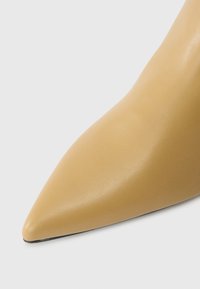 Δείκτης πέλματος από μπεζ δερμάτινο παπούτσι με λεία υφή σε λευκό φόντο.