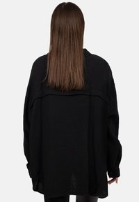 Camicia nera oversize realizzata in tessuto testurizzato. Presenta una vestibilità ampia, maniche lunghe e un sottile scollo a coste, che si estende fino a metà fianchi.