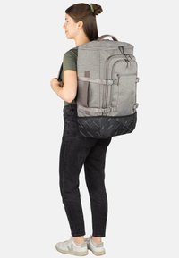 Grauer Rucksack aus Stoff mit mehreren Fächern, verstellbaren Riemen und schwarzem Bodenbereich mit wiederholtem Logomuster.