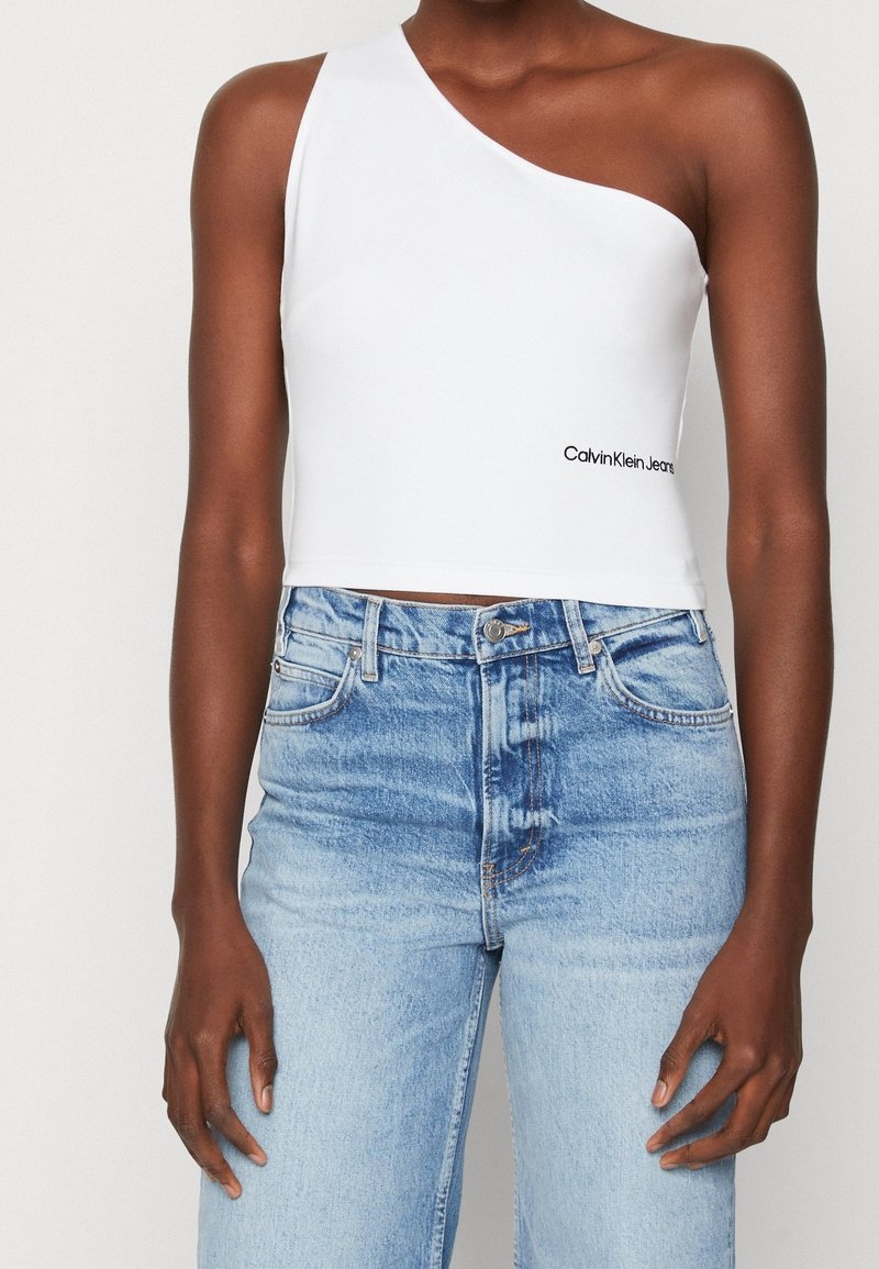 Weißes, trägerloses Crop-Top aus glattem Stoff, kombiniert mit hellblauen, hochschnittigen Jeans mit leichter Ausbleichung und klassischem Fünf-Taschen-Design.