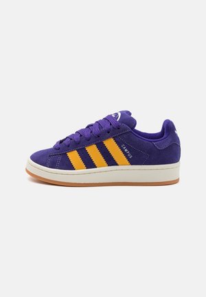 Lila Wildleder-Sneaker mit gelben Streifen, weißer Zwischensohle, Gummilaufsohle und lila Schnürsenkeln, mit der Aufschrift „Campus“ an der Seite.