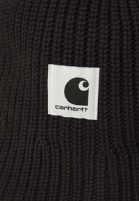 Svart strikket lue med tykk ribbestruktur og et hvitt merke med Carhartt-logoen og navnet i svart skrift.