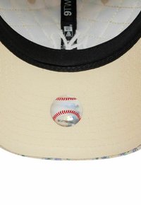 Baseballkappe mit einer cremefarbenen Krone, einem schwarzen Schirm und floralen Akzenten am Rand. Enthält einen runden holografischen Aufkleber.