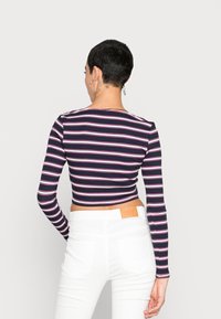 Top cropped às riscas de manga longa em azul-marinho com riscas brancas e rosas, combinado com jeans brancos de cintura alta. Apresenta um decote redondo.