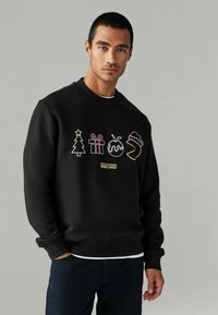 Sudadera negra con íconos festivos bordados: un árbol de Navidad, regalos, un pudín y un gorro. Puños y cuello de canalé.