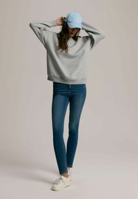 Szary sweter z luźnym krojem, niebieska czapka z daszkiem i niebieskie dżinsy z wysokim stanem, w połączeniu z białymi trampkami. Gładkie faktury na całej powierzchni.