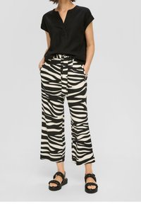 Haut noir à manches courtes avec un décolleté en V, associé à un pantalon à jambes larges imprimé zèbre en noir et crème. Des sandales épaisses noires complètent la tenue.