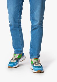 Sneaker multicolori con sezioni blu, verdi e grigie. Materiali in rete e texture, con lacci beige e suola in gomma.