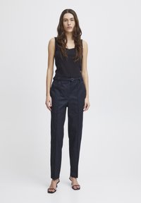 Canottiera nera con scollatura quadrata, abbinata a pantaloni navy a vita alta con cintura intrecciata e gamba affusolata.