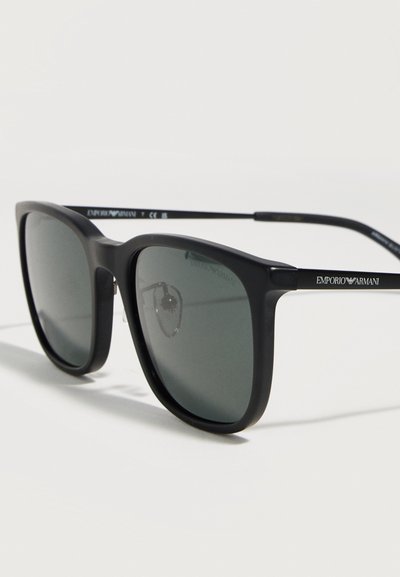 Μαύρα ορθογώνια γυαλιά ηλίου Emporio Armani με σκουρόχρωμους φακούς και λεπτά πλαίσια πάνω σε ανοιχτή επιφάνεια.