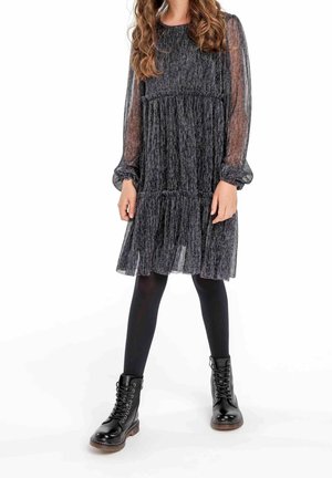 Sort og sølv flerlaget kjole med gennemsigtige lange ærmer, kombineret med sorte ankelstøvler. Kjolen har et tekstureret, stribet mønster.