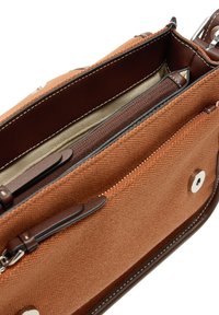 Brązowa torebka z płótna o teksturowanym wnętrzu, z wieloma przegródkami, brązowymi skórzanymi akcentami i srebrnymi elementami wykończenia.