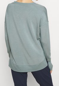 Felpa blu-verde chiaro con vestibilità rilassata, maniche raglan e scollo rotondo. Tessuto morbido con dettagli di cucitura visibili.